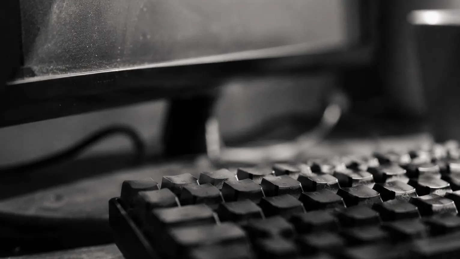 Teclado e monitor sobre uma bancada de trabalho, em foco raso.